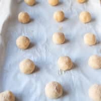 Sugar cookie balls on a baking sheet each rolled in vanilla sugar ready to bake in the oven