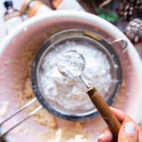 A hand sifting the flour and cornstarch into the bowl of sugar cookie dough