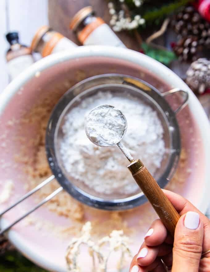 A hand sifting the flour and cornstarch into the bowl of sugar cookie dough