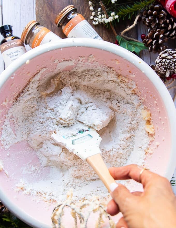 A spatula is used to blend in the dry ingredients into the butter mixture to make the sugar cookie dough without over mixing 
