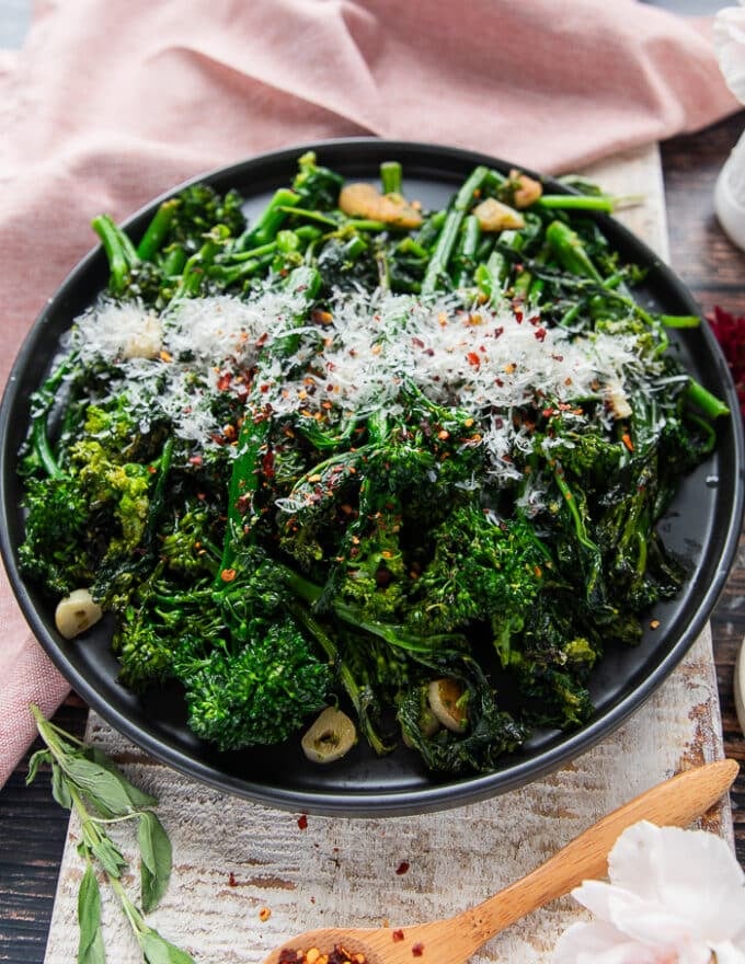 Side view of a plate of cooked rapini with lots of parmesan on top and chilli flakes