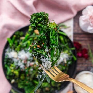A hand holding a closeup of cooked broccoli rabe showing the perfect green color, and soft texture with a sprinkle of chilli flakes and parmesan cheese