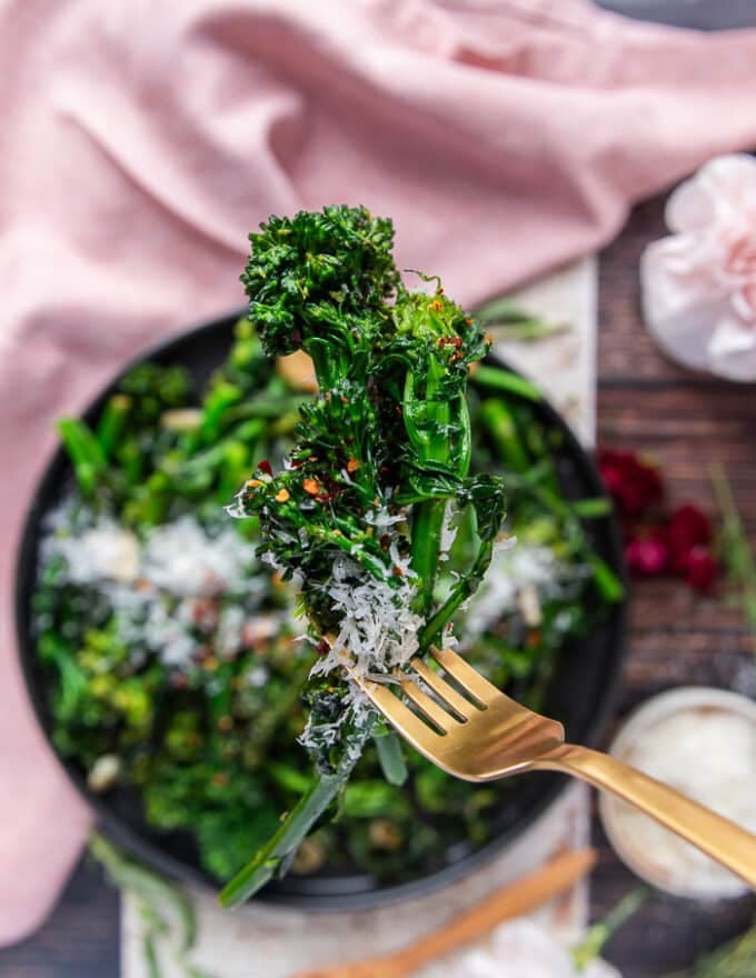 A hand holding a closeup of cooked broccoli rabe showing the perfect green color, and soft texture with a sprinkle of chilli flakes and parmesan cheese