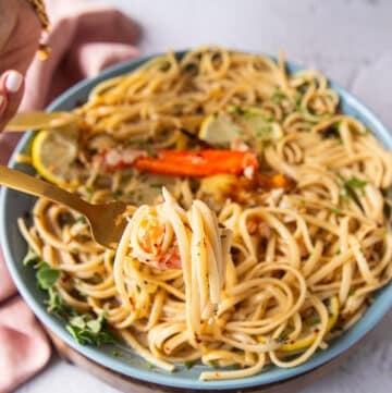 A hand holding a fork and showing close up some crab tossed in pasta with a lemon garlic zesty sauce