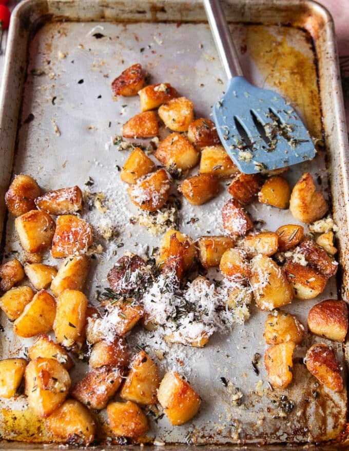 rosemary, minced garlic and parmesan are added to the ready potatoes in the baking sheet for seasoning and flavoring them 
