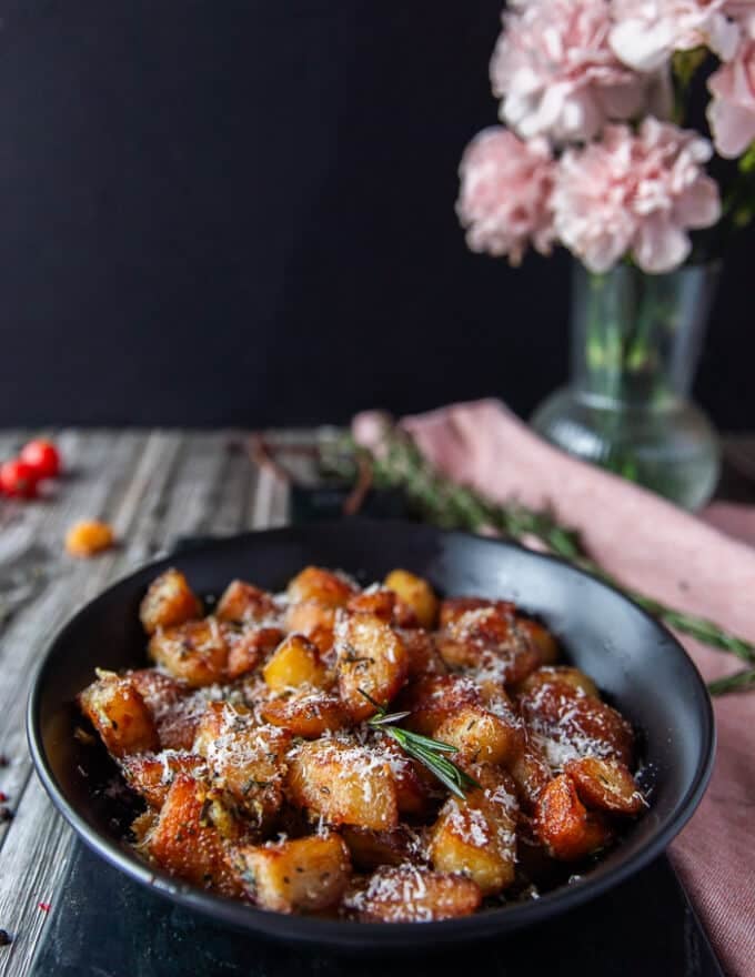 crispy potatoes on a plate sprinkled with extra parmesan cheese, and fresh rosemary sprigs served and ready 