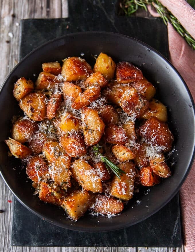 Top view close up of crispy potatoes showing the deep golden color and crisp outside of the roasted potatoes and some rosemary and parmesan on top