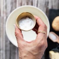 A hand holding a small bowl of baking soda and pouring it into the pot of boiling water