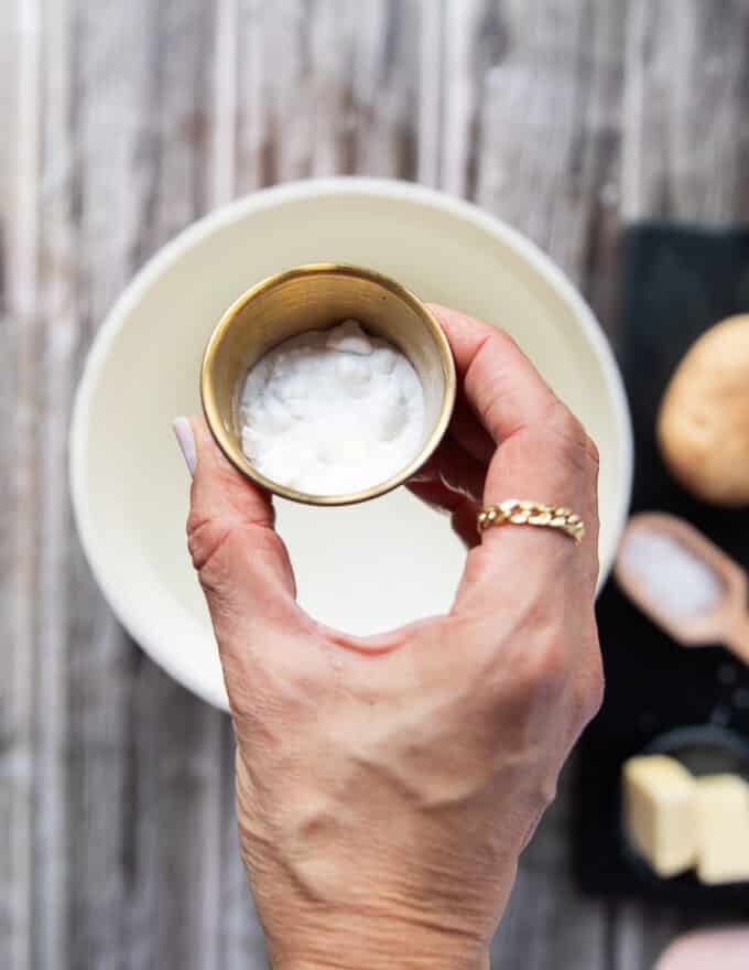 A hand holding a small bowl of baking soda and pouring it into the pot of boiling water 
