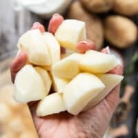 A hand holding peeled and cubed potatoes cut into 1 inch cubes ready to boil