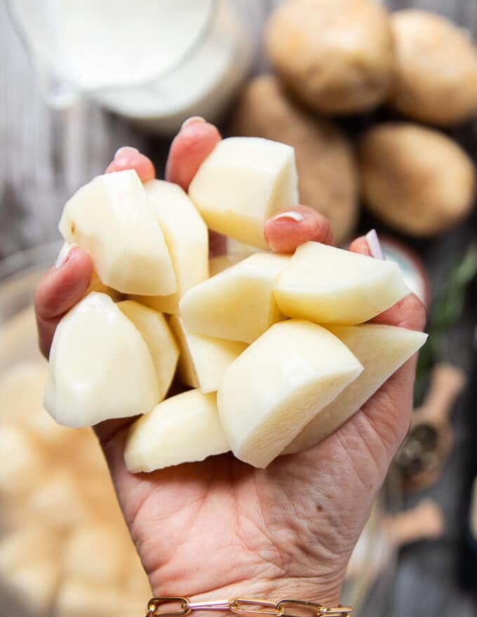 A hand holding peeled and cubed potatoes cut into 1 inch cubes ready to boil 