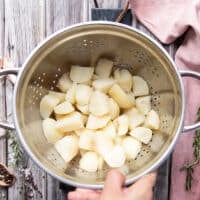 A hand holding a colander with the boiled potatoes drained and ready