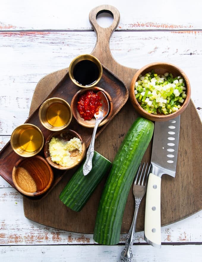 ingredients for the easy cucumber salad including two large cucumbers, minced scallions, a bowl of soy sauce, a bowl of honey, a bowl of rice vinegar, a bowl of grated ginger and garlic and a bowl of chilli paste