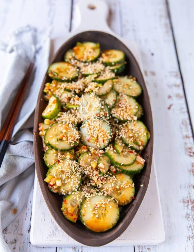 A whole plate of cucumber salad sprinkled with sesame seeds and some chopsticks for serving on the side