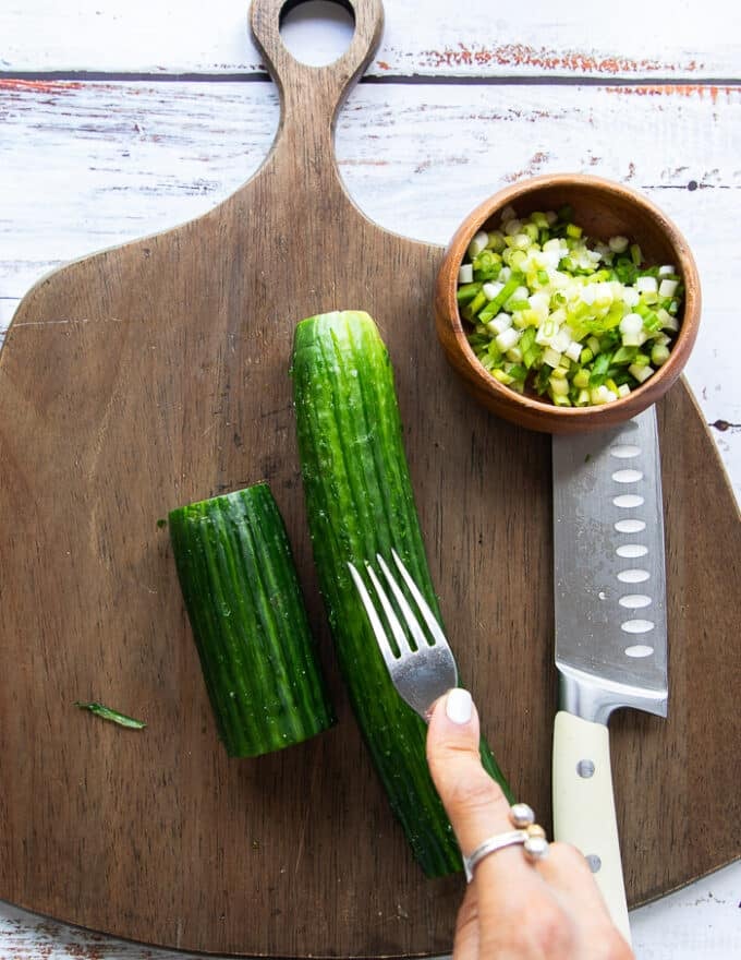 A hand using a fork to scorch the cucumbers for them to absorb maximum dressing