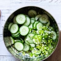 The sliced cucumbers and scallions added into the salad bowl of the dressing