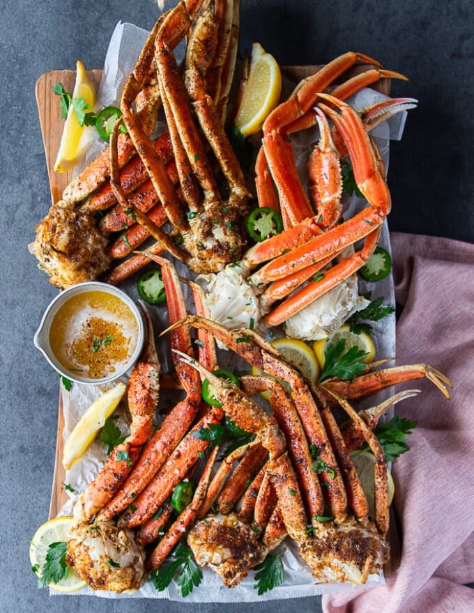 A whole board of cooked crab legs different ways, the grilled, baked, air fried and steamed crab legs surrounded by a bowl of melted butter