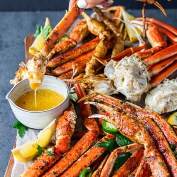 A hand dipping a cooked crab leg into a bowl of melted butter and the butter dripping from it close up