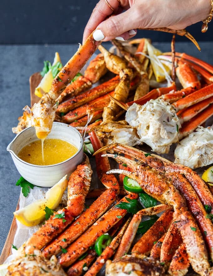 A hand dipping a cooked crab leg into a bowl of melted butter and the butter dripping from it close up