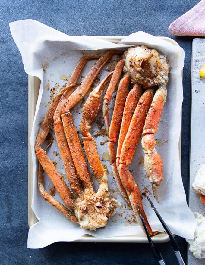 crab legs on a baking sheet seasoned with cajun spice blend and drizzled with olive oil.