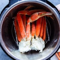 A set of crab legs placed in an instant pot steamer with lemon, bay leaf and garlic at the water for steaming