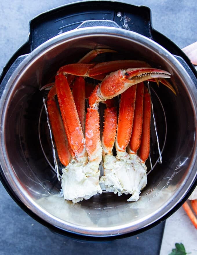 A set of crab legs placed in an instant pot steamer with lemon, bay leaf and garlic at the water for steaming
