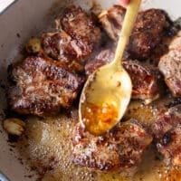 A spoon basting some butter from the skillet over the lamb chops to infuse them and cook them