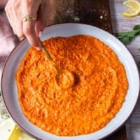 A hand spreading a layer of romesco sauce over the plate