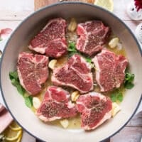 Garlic cloves and fresh herbs and lemon slices are added to the same skillet as the lamb chops for flavor