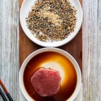 The ahi tuna fish is soaked into a plate of soy sauce as a first step to marinate the fish