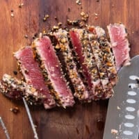 A knife slicing the ahi tuna into a 1/4th inch thick slices on a cutting board