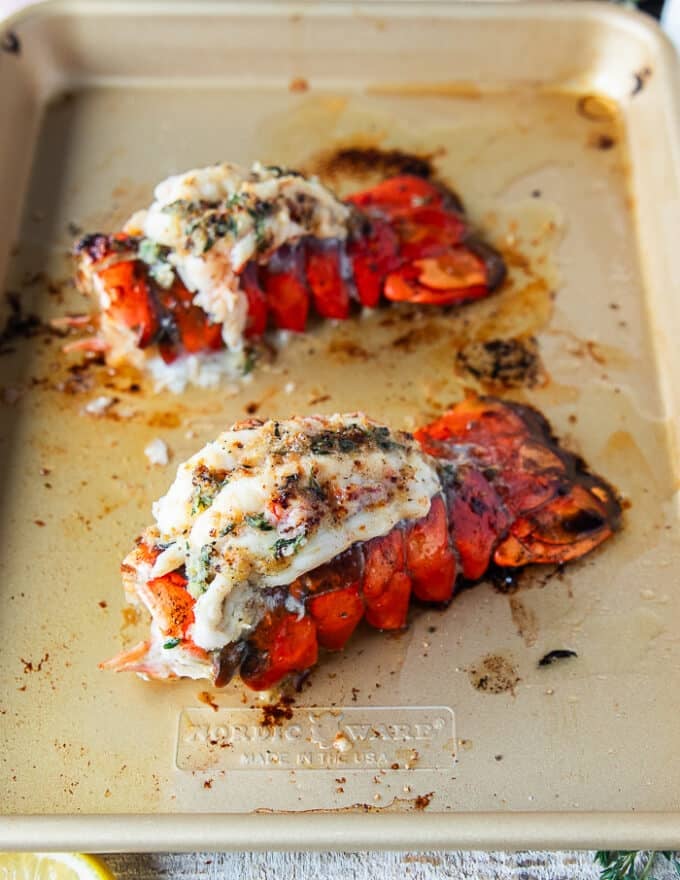 lobster tails on a baking sheet broiled and slathered in herb butter