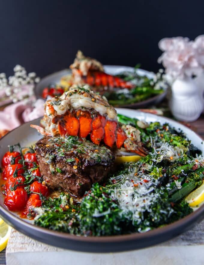 A full plate of fillet mignon cooked perfectly and a lobster tail on tops with herb butter drizzling, some rapini on the side, lemon wedges and parmesan cheese for the final surf and turf plate