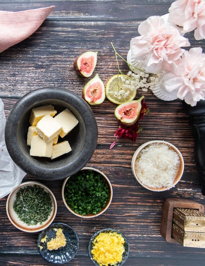 Herb butter ingredients for the surf and turf including soft butter, lemon zest, fresh herbs in a bowl, some parmesan in a bowl, salt and pepper and minced garlic in a bowl