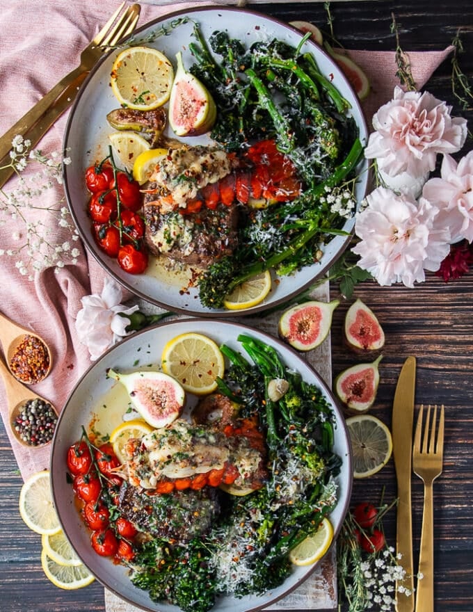 two plates of surf and turf each served with a side of broccoli rabe, some lemon slices and tomatoes on the vine along with the lobster and fillet mignon