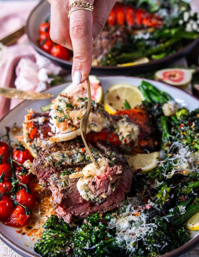 A hand holding a fork with a piece of lobster, a piece of fillet mignon and showing close up the bite