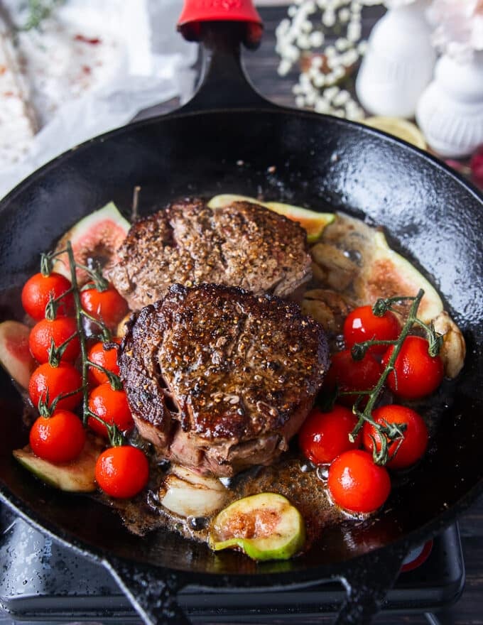Whole garlic cloves, tomatoes on the vine and herbs are added to the cast iron skillet