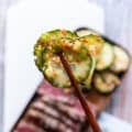 a hand holding a cucumber using chopsticks up close showing the texture and marinade of the cucumber salad