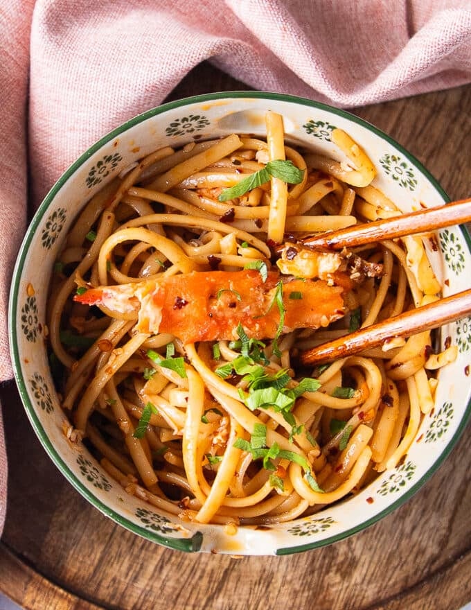 Large Crab meat added over a bowl of creamy chili crab pasta and two chopsticks on the side 