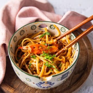 two chopsticks over a bowl of creamy chili crab pasta with a large chunk of cooked crab over the chili tossed pasta
