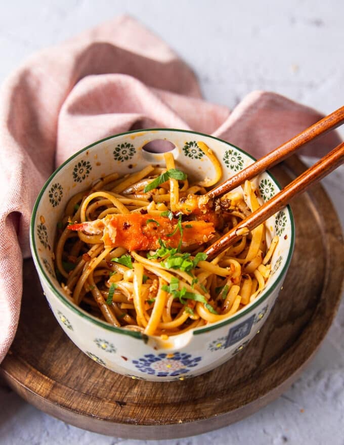 two chopsticks over a bowl of creamy chili crab pasta with a large chunk of cooked crab over the chili tossed pasta 