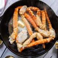 fresh crab legs cooking in a skillet with butter, salt and pepper