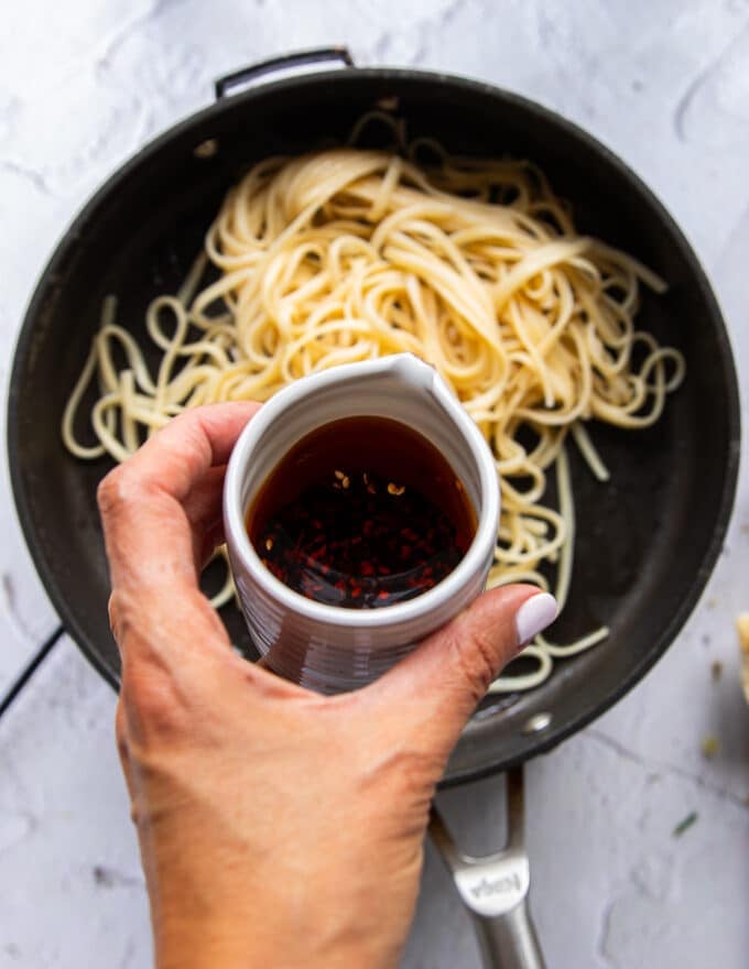 A hand pouring the spicy chili oil over cooked pasta to make chili crab pasta