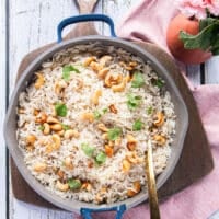 Coconut rice served with fresh cilantro leaves on top and extra cashews