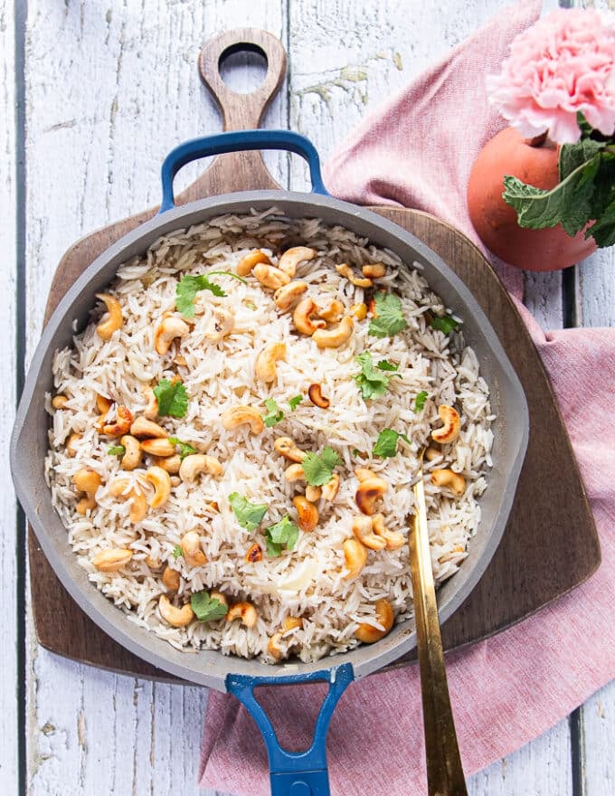Coconut rice served with fresh cilantro leaves on top and extra cashews