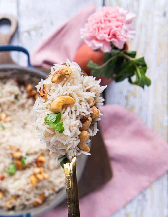 A spoon holding off some coconut rice close up showing how fluffy and well cooked it is with some toasted cashews 