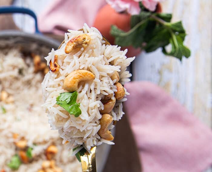 A spoon holding off some coconut rice close up showing how fluffy and well cooked it is with some toasted cashews