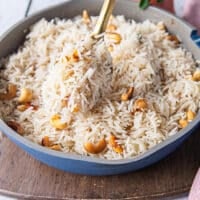 A hand fluffing up the cooked coconut rice close up showing how every rice is so fluffy and the cashews are studded within the coconut rice