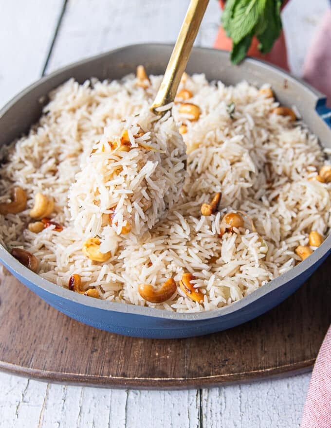 A hand fluffing up the cooked coconut rice close up showing how every rice is so fluffy and the cashews are studded within the coconut rice 