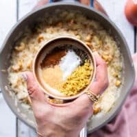 A hand holding a small plate of seasoning to add in to the rice